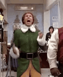 A Man In A Green Elf Costume Is Standing In A Room With His Mouth Wide Open . GIF