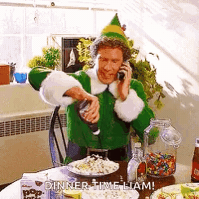 A Man In A Green Elf Costume Is Talking On A Cell Phone While Pouring Popcorn Into A Bowl . GIF