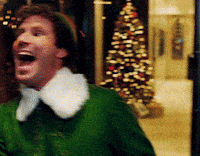 A Man In A Green Elf Costume With A White Collar Is Laughing In Front Of A Christmas Tree GIF