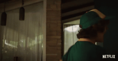 A Man In A Green Hat Is Standing In Front Of A Brick Wall With A Netflix Logo Behind Him GIF