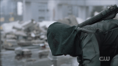 A Man In A Green Hooded Jacket Is Holding A Sword With The Letters Cw On The Bottom GIF
