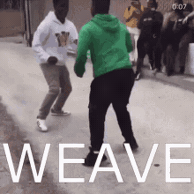 A Man In A Green Hoodie Is Dancing With Another Man In A White Hoodie On A Street . GIF