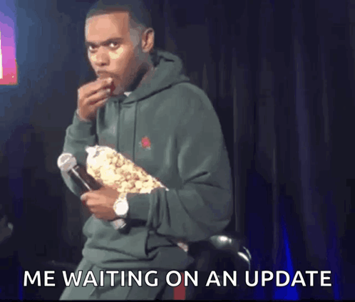 A Man In A Green Hoodie Is Eating Popcorn And Holding A Microphone . GIF