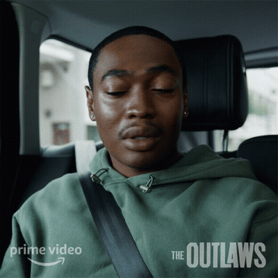 A Man In A Green Hoodie Is Sitting In A Car With His Eyes Closed And The Words The Outlaws On The Side GIF