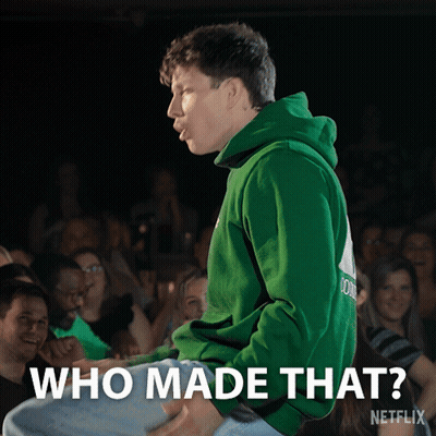 A Man In A Green Hoodie Is Sitting In Front Of A Crowd With The Words " Who Made That " Above Him GIF
