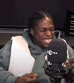 A Man In A Green Hoodie Is Sitting In Front Of A Microphone . GIF