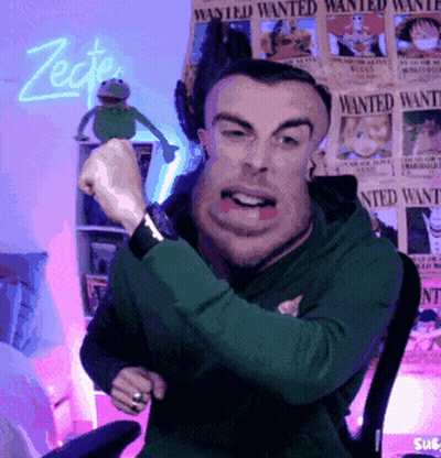 A Man In A Green Hoodie Is Sitting In Front Of Wanted Posters GIF