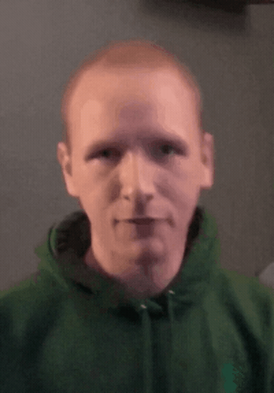 A Man In A Green Hoodie Looks At The Camera . GIF