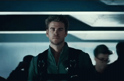 A Man In A Green Jacket And Black Vest Is Standing In A Crowded Room . GIF