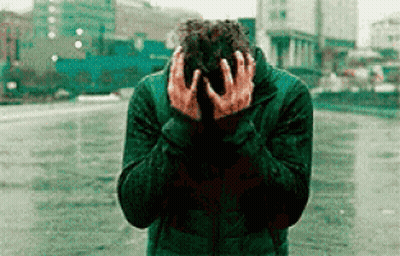 A Man In A Green Jacket Is Covering His Face With His Hands . GIF