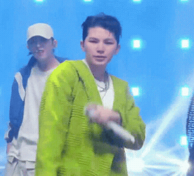 A Man In A Green Jacket Is Holding A Microphone While Standing On A Stage . GIF