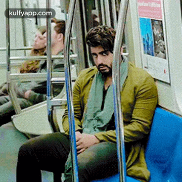 A Man In A Green Jacket Is Sitting On A Blue Bench On A Subway Train . GIF