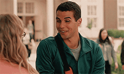 A Man In A Green Jacket Is Smiling And Talking To A Woman . GIF
