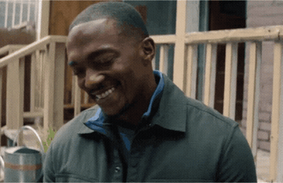 A Man In A Green Jacket Is Smiling In Front Of A Railing GIF