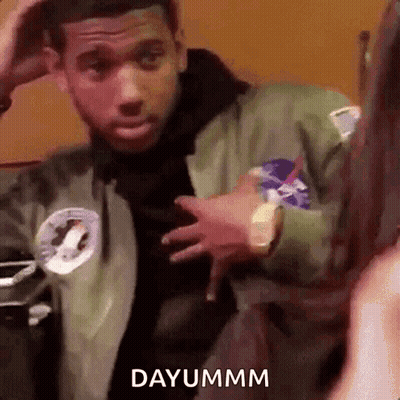 A Man In A Green Jacket Is Standing In Front Of A Woman And Holding His Hand To His Head . GIF