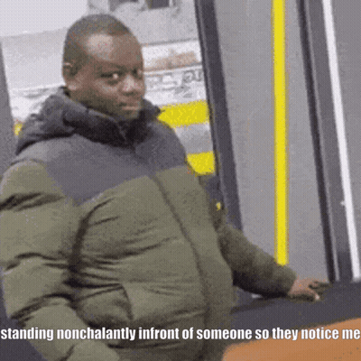 A Man In A Green Jacket Is Standing Nonchalantly In Front Of Someone So They Notice Me GIF