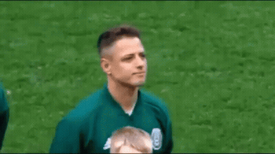 A Man In A Green Jacket Is Standing On A Soccer Field And Smiling . GIF