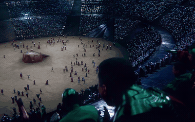 A Man In A Green Jacket Looks At A Crowd Of People GIF