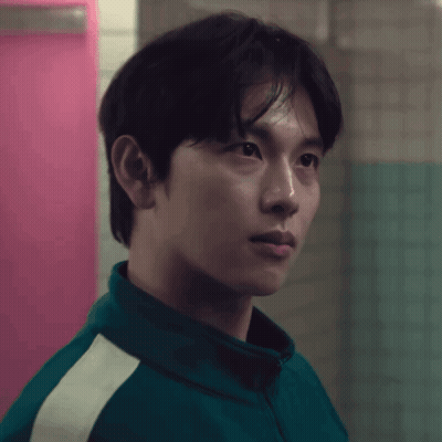 A Man In A Green Jacket Stands In Front Of A Pink Wall GIF