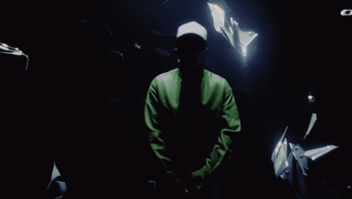 A Man In A Green Jacket Stands In The Dark GIF