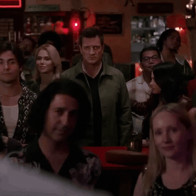 A Man In A Green Jacket Stands In The Middle Of A Crowd GIF