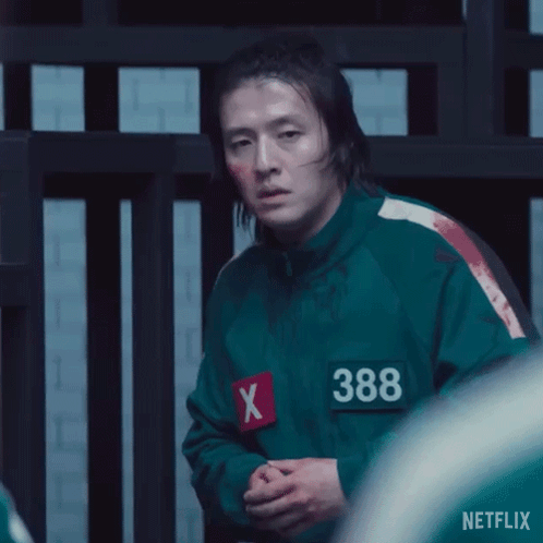 A Man In A Green Jacket With A Red X On His Chest Is Standing In Front Of A Fence . GIF