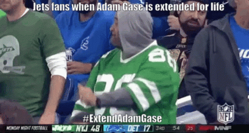 A Man In A Green Jets Jersey Is Sitting In A Stadium GIF