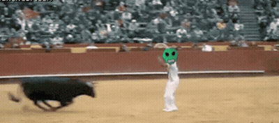 A Man In A Green Mask Stands In Front Of A Bull In A Bullring GIF