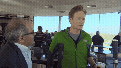 A Man In A Green North Face Jacket Talks To Another Man In A Suit GIF