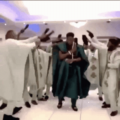 A Man In A Green Robe Is Dancing With A Group Of Men In White Robes . GIF