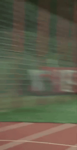 A Man In A Green Shirt And Black Shorts Is Standing On A Track GIF