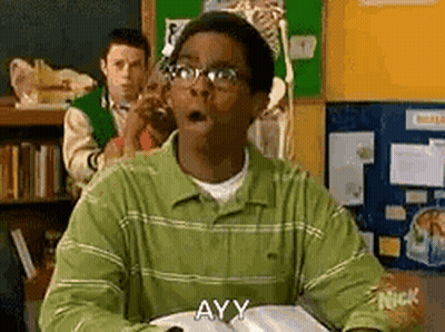 A Man In A Green Shirt And Glasses Is Sitting At A Desk In A Classroom With His Mouth Open . GIF