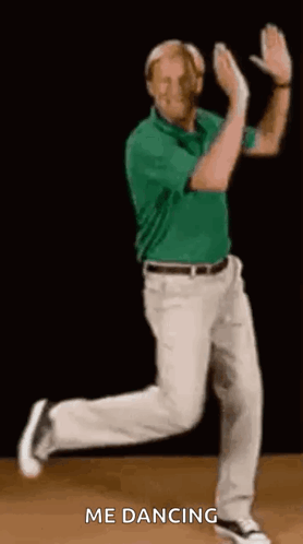 A Man In A Green Shirt And Khaki Pants Is Dancing On A Wooden Floor . GIF