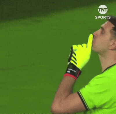 A Man In A Green Shirt And Yellow Gloves Is Making A Shhh Gesture . GIF