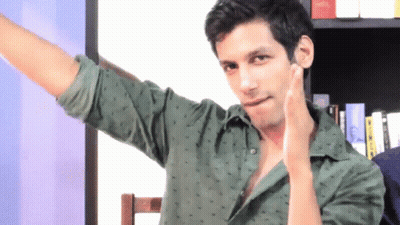 A Man In A Green Shirt Has His Arm Outstretched In Front Of A Bookshelf GIF