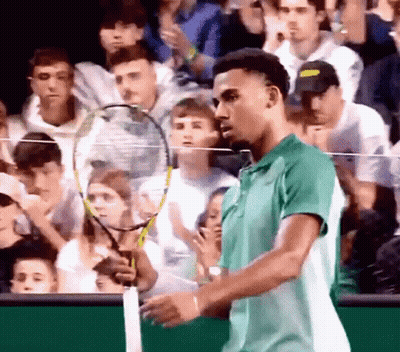 A Man In A Green Shirt Holds A Tennis Racket In Front Of A Crowd GIF