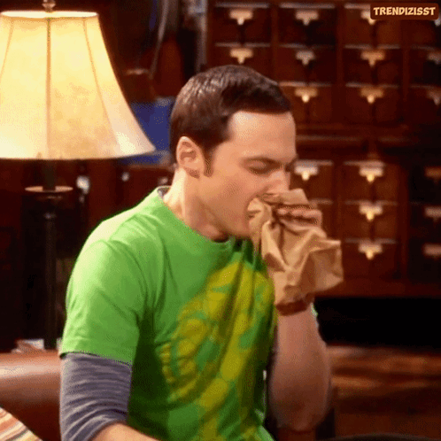 A Man In A Green Shirt Is Blowing His Nose Into A Paper Bag .. GIF