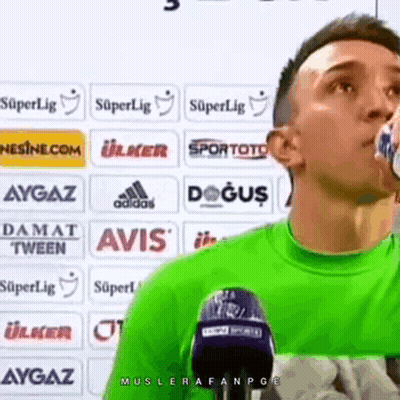 A Man In A Green Shirt Is Drinking Water From A Bottle . GIF