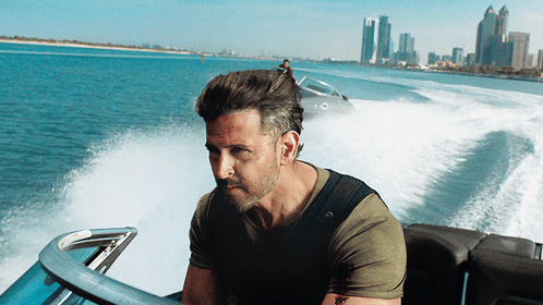 A Man In A Green Shirt Is Driving A Boat In The Ocean GIF