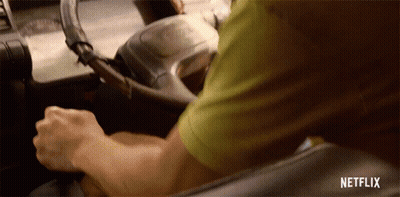 A Man In A Green Shirt Is Driving A Car With Netflix Written On The Bottom Of The Screen GIF