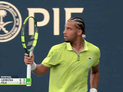 A Man In A Green Shirt Is Holding A Tennis Racquet In Front Of A Sign That Says " It " GIF