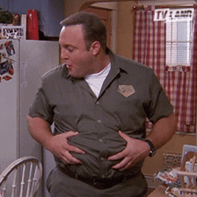 A Man In A Green Shirt Is Holding His Belly In A Kitchen . GIF