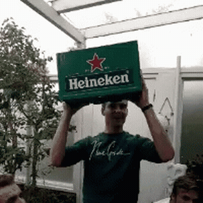 A Man In A Green Shirt Is Holding Up A Box Of Heineken GIF