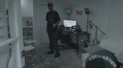 A Man In A Green Shirt Is Laying On The Floor Next To A Broken Monitor . GIF