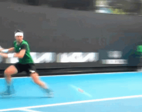 A Man In A Green Shirt Is Playing Tennis On A Court GIF