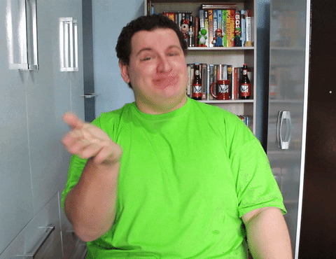A Man In A Green Shirt Is Pointing At Something In Front Of A Shelf With Books On It GIF