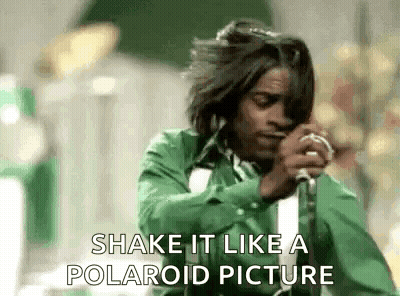A Man In A Green Shirt Is Singing Into A Microphone And Saying Shake It Like A Polaroid Picture . GIF