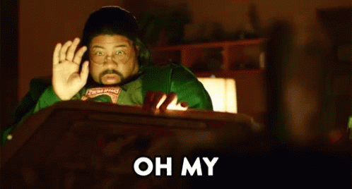 A Man In A Green Shirt Is Sitting At A Table In Front Of A Computer Screen And Waving . GIF