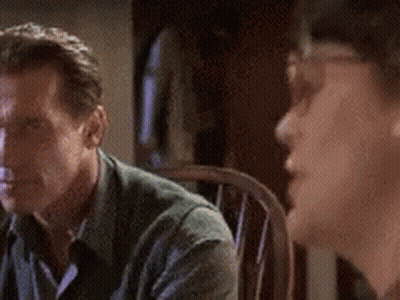 A Man In A Green Shirt Is Sitting In A Chair Looking At Another Man . GIF