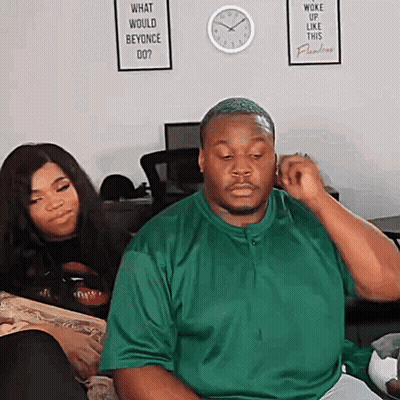 A Man In A Green Shirt Is Sitting In Front Of A Sign That Says What Would Beyonce Do? GIF